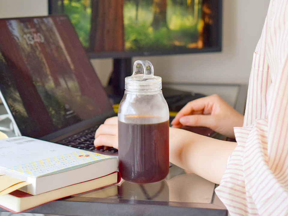 ノートパソコンで作業する人のそばにアイスコーヒーが置かれている様子
