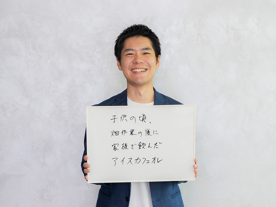 ボードに「子供の頃、畑作業の後に家族で飲んだアイスカフェオレ」と書かれているのを持っている様子