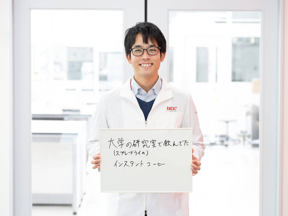 「大学の研究室で飲んでた（スプレードライの）インスタントコーヒー」と書かれたボードを持っている男性