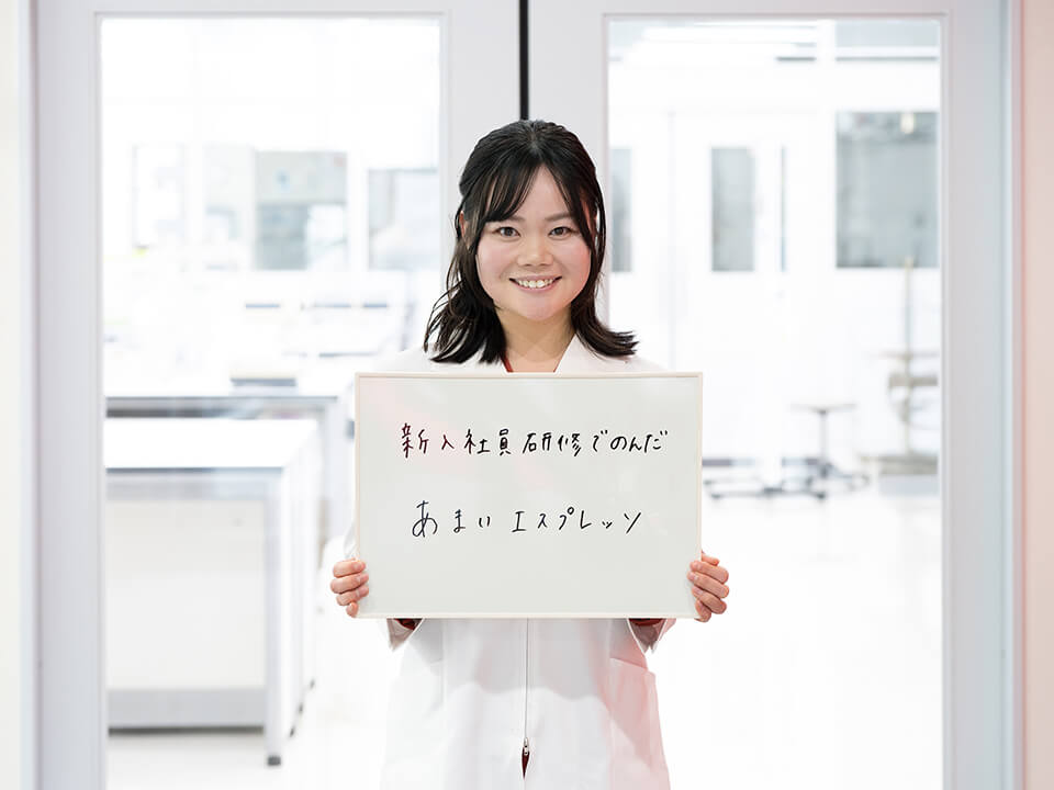 「新入社員間修でのんだあまいエスプレッソ」と書かれたボードを持っている女性